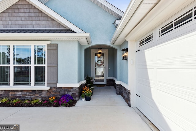 doorway to property with a garage, stone siding, metal roof, a standing seam roof, and stucco siding