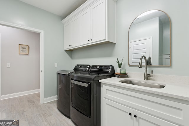 washroom with washing machine and clothes dryer, cabinet space, a sink, light wood-type flooring, and baseboards