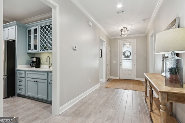 entrance foyer with visible vents, baseboards, light wood-type flooring, wet bar, and crown molding