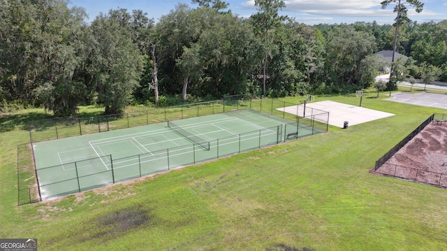 view of tennis court with fence and a yard