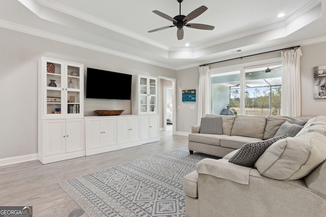 living room featuring a ceiling fan, baseboards, a tray ceiling, light wood finished floors, and crown molding