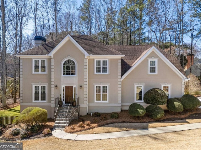 colonial house with a shingled roof, a chimney, fence, and stucco siding