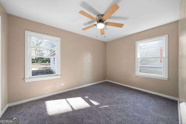 carpeted spare room featuring a ceiling fan, baseboards, and a wealth of natural light