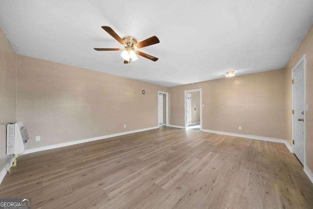 unfurnished living room with heating unit, ceiling fan, baseboards, and wood finished floors