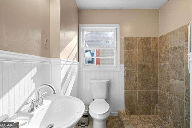 bathroom featuring a wainscoted wall, tiled shower, a sink, and toilet