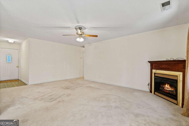 unfurnished living room featuring a textured ceiling, ceiling fan, carpet floors, visible vents, and a glass covered fireplace