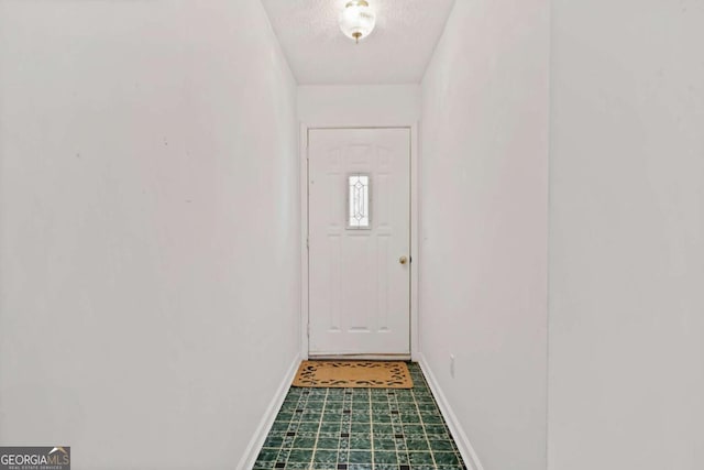 doorway to outside with baseboards, a textured ceiling, and tile patterned floors