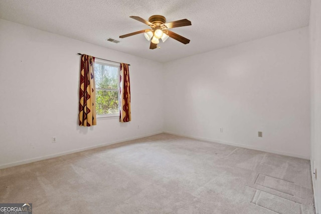 spare room featuring light carpet, ceiling fan, visible vents, and a textured ceiling