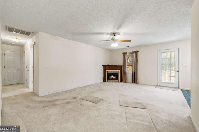 unfurnished living room with a textured ceiling, visible vents, a ceiling fan, a lit fireplace, and carpet