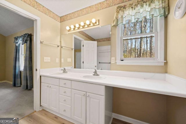 full bathroom with double vanity, a textured ceiling, a sink, and wood finished floors