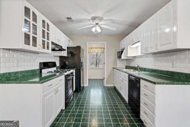 kitchen featuring white cabinets, dark countertops, under cabinet range hood, black appliances, and a sink