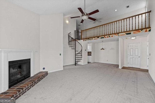 unfurnished living room with a fireplace with raised hearth, ceiling fan, visible vents, stairs, and carpet