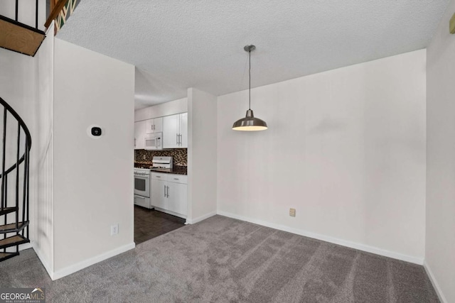 unfurnished dining area with baseboards, stairway, dark colored carpet, and a textured ceiling