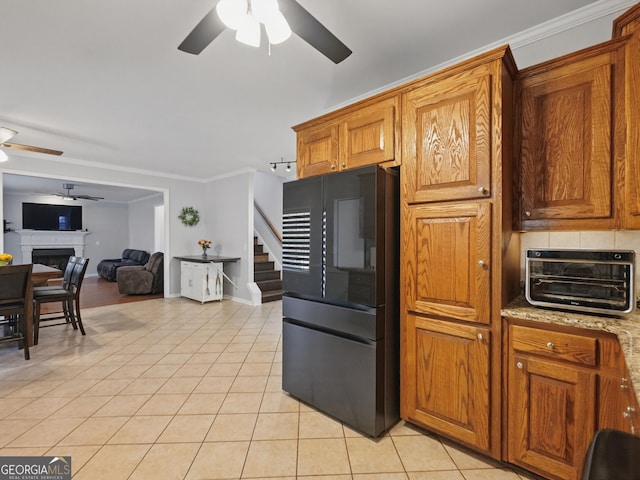 kitchen with crown molding, a fireplace, black fridge, and light tile patterned floors