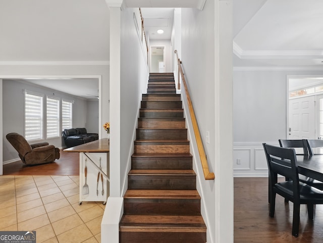 stairway with crown molding, a decorative wall, wainscoting, and tile patterned floors