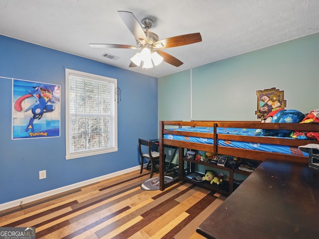 bedroom with baseboards, visible vents, ceiling fan, wood finished floors, and a textured ceiling