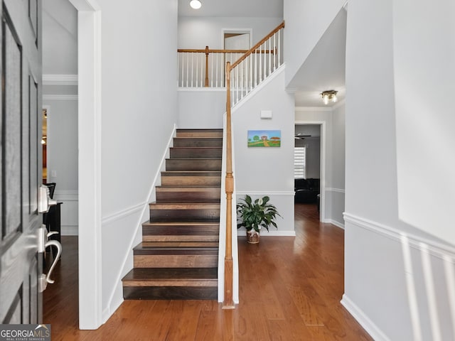 stairs featuring a high ceiling, crown molding, baseboards, and wood finished floors