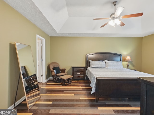 bedroom with a ceiling fan, baseboards, a tray ceiling, and wood finished floors