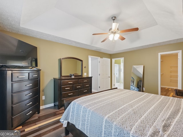 bedroom featuring visible vents, a ceiling fan, dark wood finished floors, baseboards, and a raised ceiling