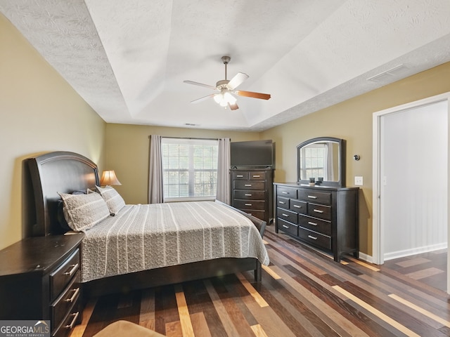 bedroom featuring baseboards, visible vents, dark wood finished floors, a tray ceiling, and a textured ceiling