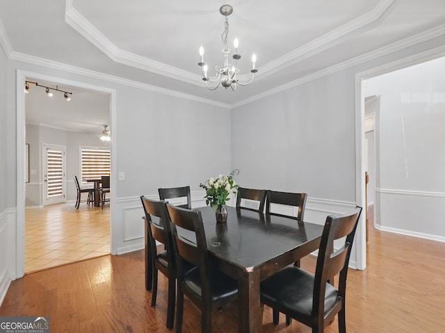 dining space with light wood finished floors, a raised ceiling, a decorative wall, an inviting chandelier, and ornamental molding