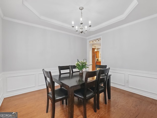 dining space with a chandelier, a tray ceiling, wood finished floors, and ornamental molding