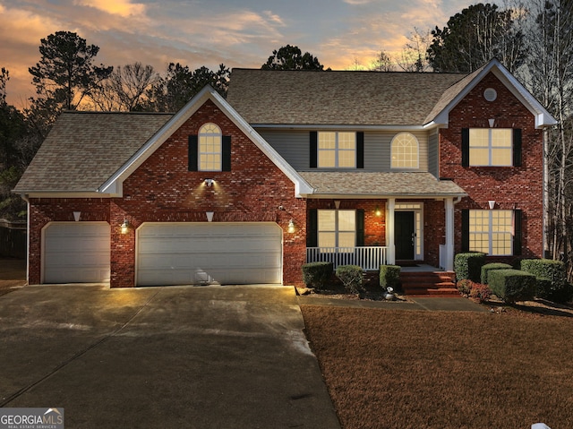 traditional-style home featuring brick siding, a shingled roof, covered porch, concrete driveway, and an attached garage