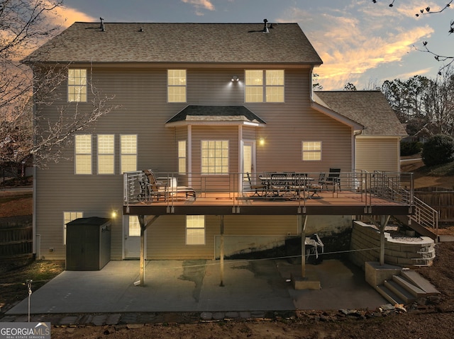 back of house at dusk with a deck, a patio, and a shingled roof