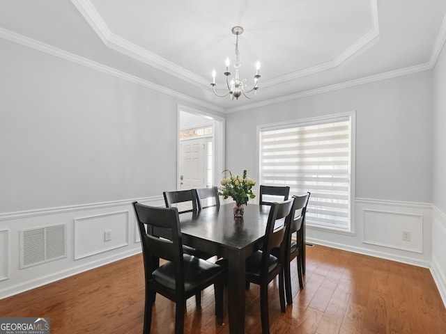 dining area featuring visible vents, a wainscoted wall, ornamental molding, hardwood / wood-style floors, and a chandelier