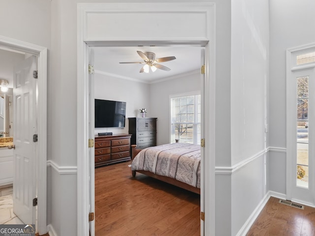 bedroom featuring crown molding, visible vents, ensuite bathroom, wood finished floors, and baseboards