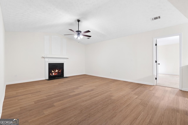 unfurnished living room featuring lofted ceiling, visible vents, a fireplace with flush hearth, ceiling fan, and light wood-type flooring