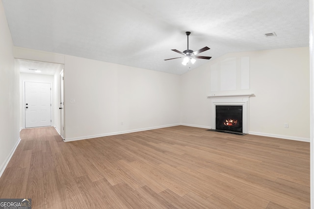 unfurnished living room featuring ceiling fan, a fireplace with flush hearth, visible vents, vaulted ceiling, and light wood finished floors