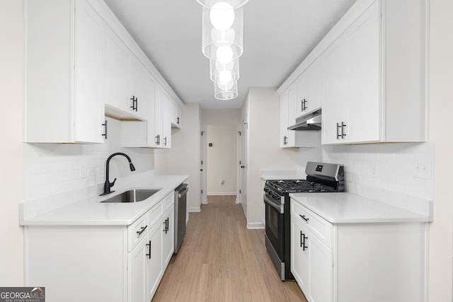 kitchen with appliances with stainless steel finishes, light countertops, under cabinet range hood, white cabinetry, and a sink