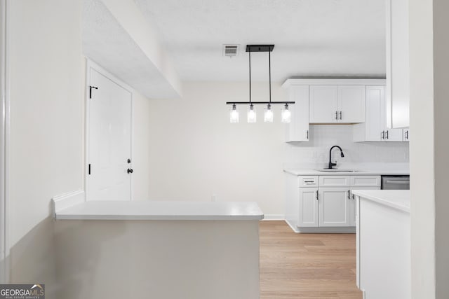 kitchen with light wood-type flooring, a sink, visible vents, and white cabinetry