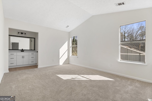 unfurnished bedroom with lofted ceiling, a textured ceiling, light colored carpet, visible vents, and baseboards