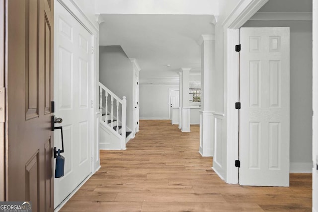 foyer featuring a decorative wall, crown molding, stairway, and light wood finished floors