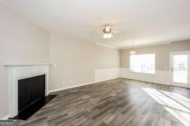 unfurnished living room featuring dark wood-style floors, a wainscoted wall, a fireplace, a decorative wall, and a ceiling fan