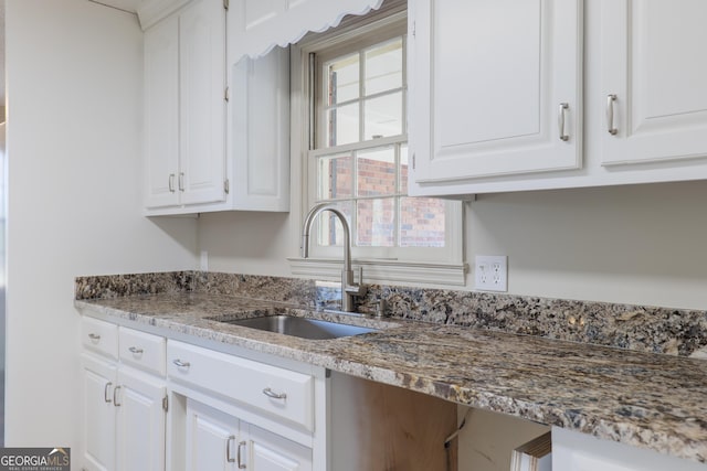 kitchen with stone counters, white cabinetry, and a sink