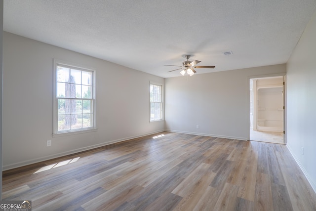 empty room with light wood-style floors, baseboards, visible vents, and a textured ceiling