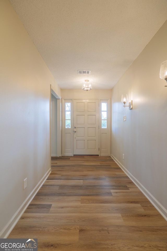 foyer entrance with visible vents, a textured ceiling, baseboards, and wood finished floors