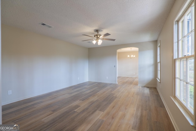 empty room with arched walkways, visible vents, a textured ceiling, wood finished floors, and ceiling fan with notable chandelier