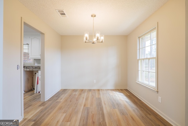 unfurnished room featuring baseboards, visible vents, a textured ceiling, light wood-style floors, and a chandelier