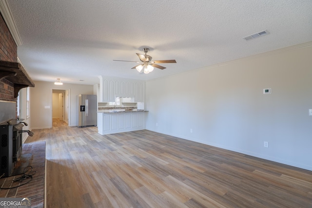 unfurnished living room with crown molding, visible vents, light wood-style floors, ceiling fan, and a textured ceiling