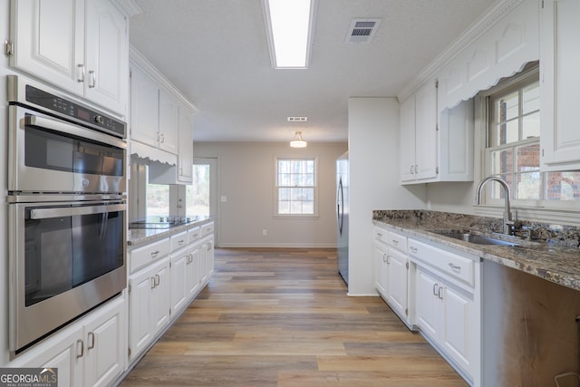 kitchen with visible vents, appliances with stainless steel finishes, white cabinetry, a sink, and light wood-type flooring