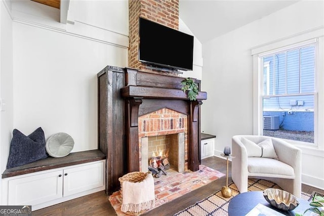 sitting room with lofted ceiling, a brick fireplace, dark wood finished floors, and baseboards