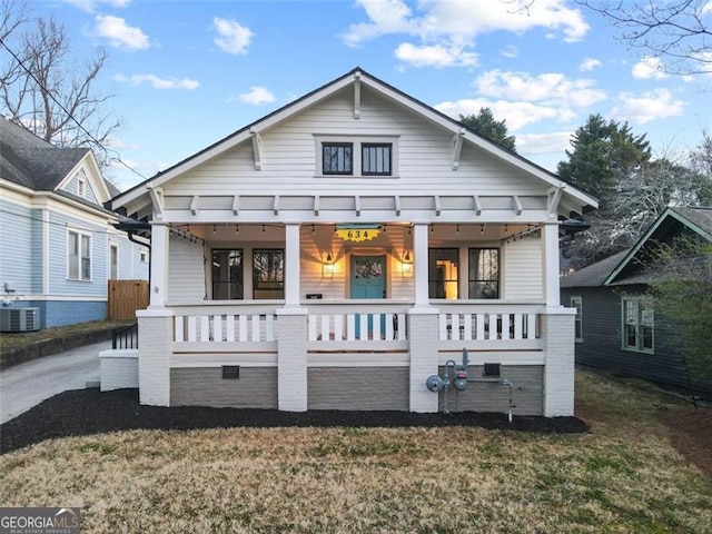 bungalow-style home with covered porch, a front yard, and central air condition unit