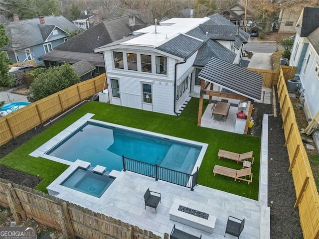 exterior space with a fenced backyard, a fire pit, a pool with connected hot tub, a yard, and a patio area