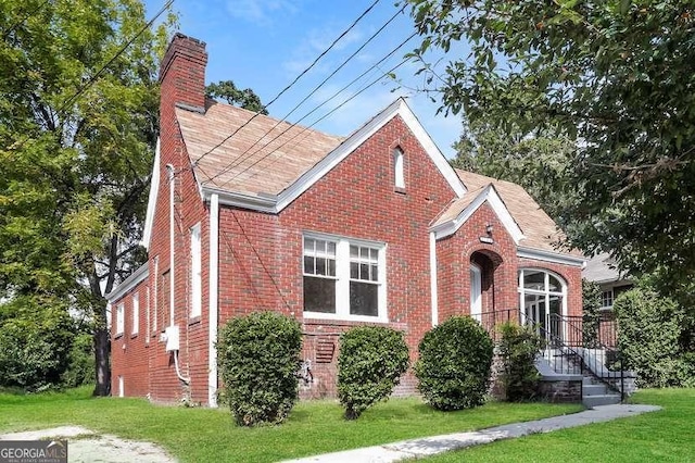 view of front of house featuring brick siding, a front lawn, a chimney, and a shingled roof