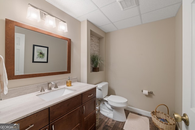 half bathroom featuring visible vents, a drop ceiling, toilet, wood finished floors, and vanity