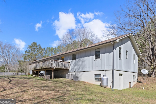 back of house with board and batten siding, a lawn, central AC unit, and a deck